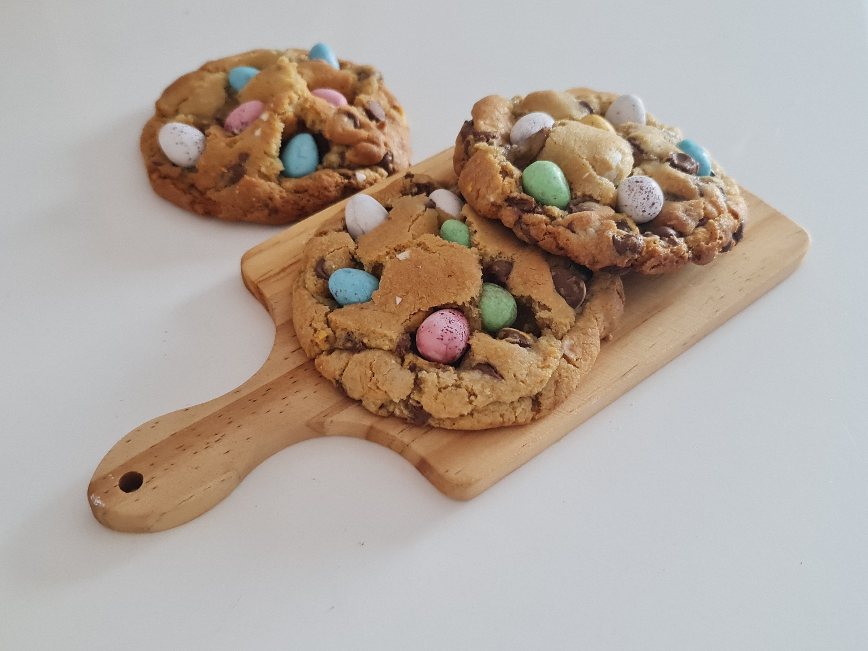 Chunky new york style cookies with M&M chocolate on a mini wooden chopping board on a white back gorund